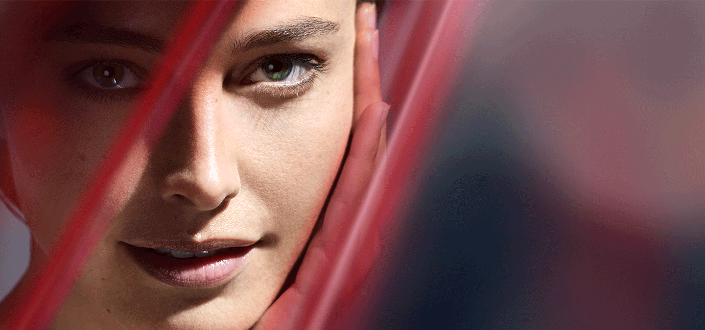 Close-up of a woman’s face, partially framed by soft red lines, with one hand gently resting on her cheek.